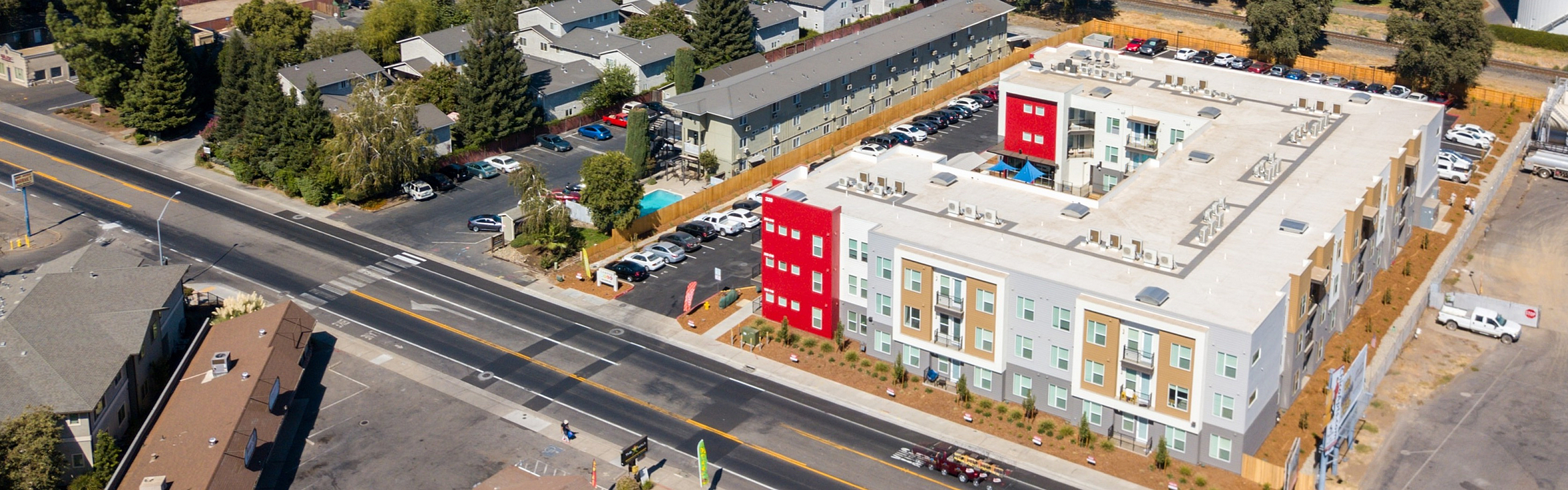 Scenic aerial view showcasing a vibrant apartment complex with colorful facades, surrounded by lush greenery and conveniently located near a school and sports facilities.