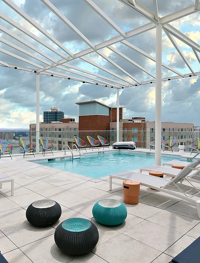 Stunning rooftop pool terrace with modern lounge chairs and vibrant city views, perfect for relaxation and entertainment.