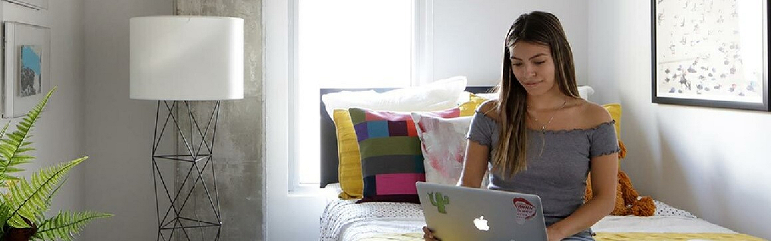 Modern cozy bedroom with stylish decor, featuring a concrete ceiling, colorful bedding, a sleek desk, and natural light streaming through the window.