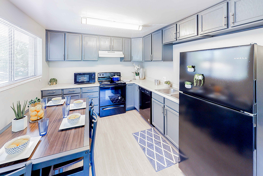 Bright, modern kitchen with sleek black appliances, elegant gray cabinetry, and a cozy dining area bathed in natural light.