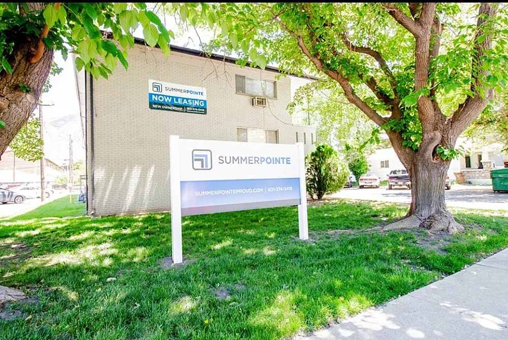 Inviting Summer Pointe apartment building with lush green surroundings and a clear leasing sign, offering modern living in a serene environment.