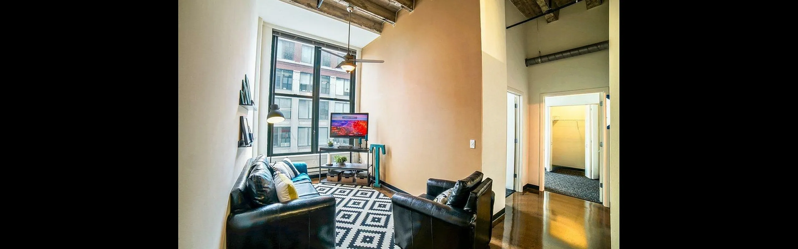 Modern living room with industrial ceiling, large window, cozy leather seating, and vibrant decor.