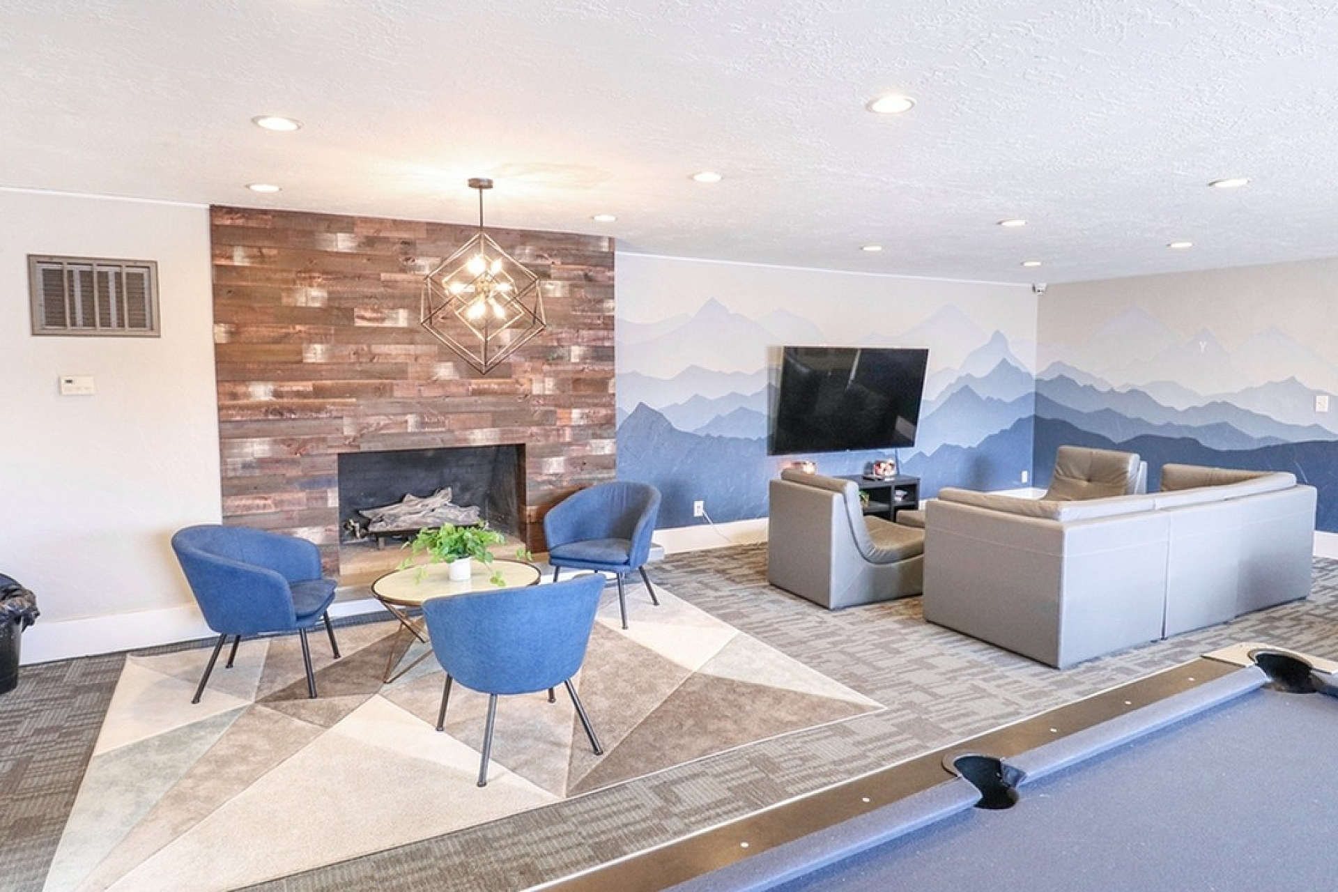 Chic lounge area featuring modern decor with a rustic fireplace, plush seating, stylish lighting, and a scenic wall mural, perfect for relaxation and entertainment.