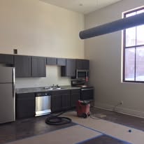Modern kitchen area with sleek dark cabinets, stainless steel appliances, and large window bringing in natural light.