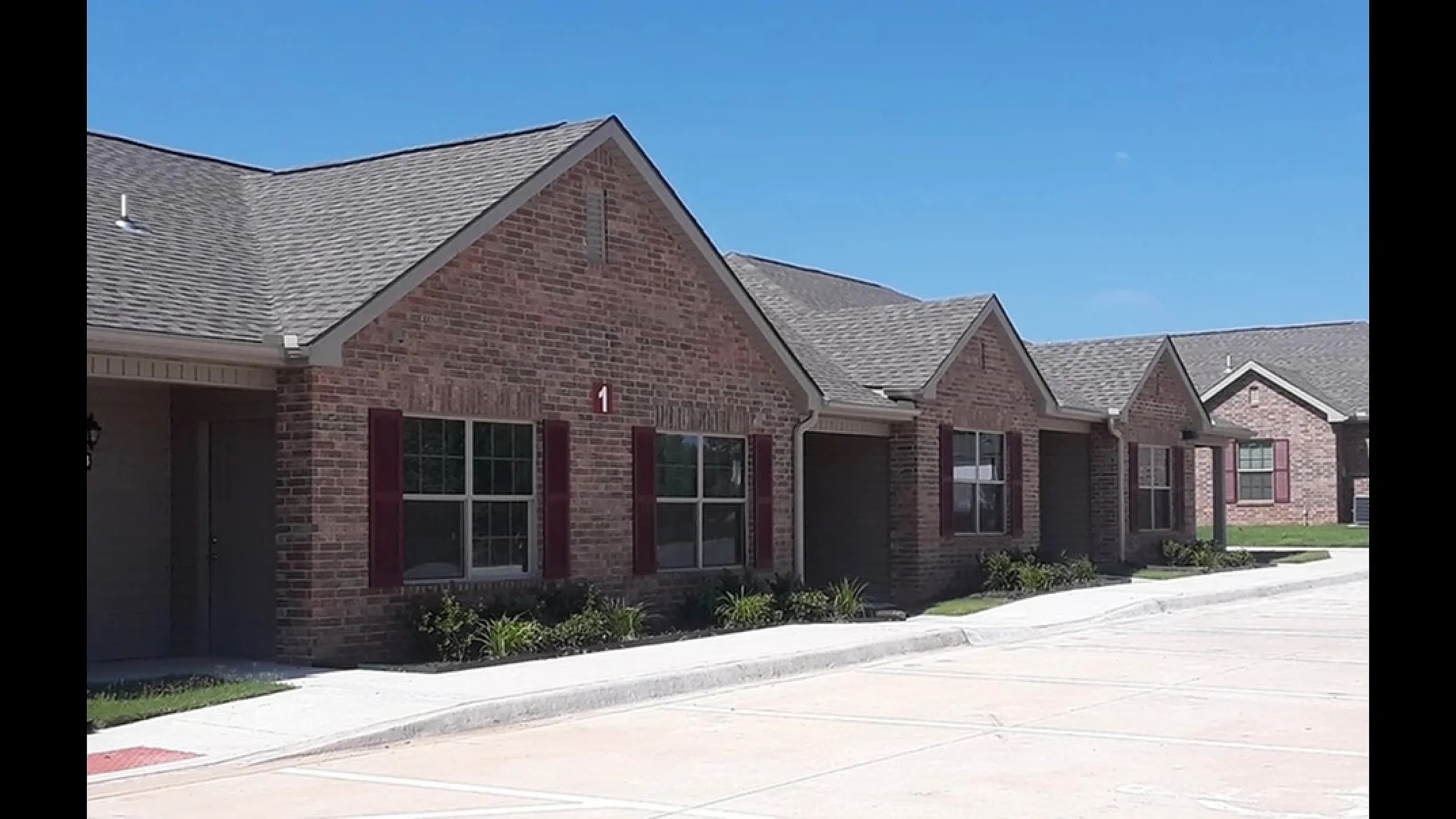 Row of charming brick residential homes with front gardens and a clear blue sky.