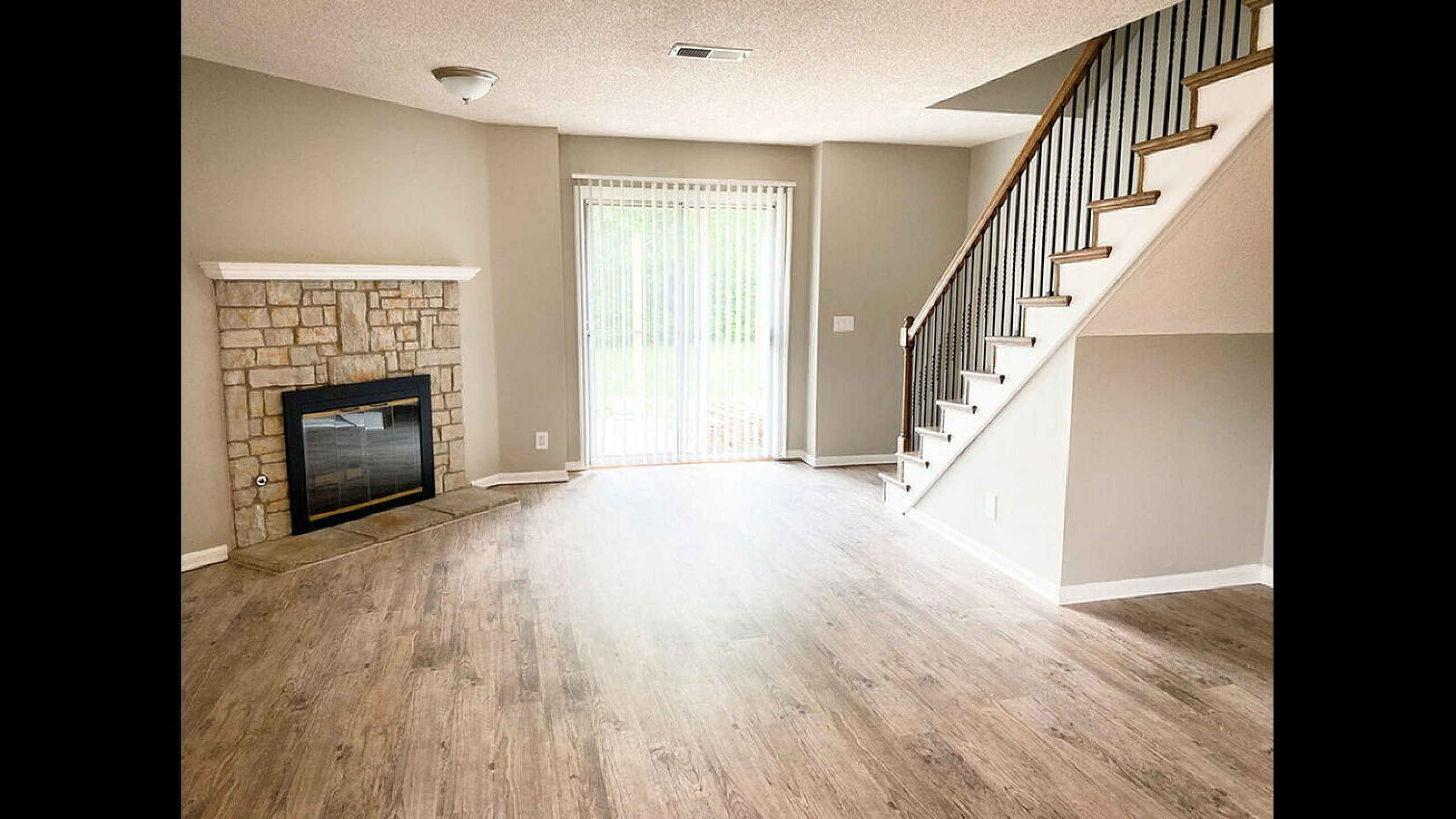 Bright living room with hardwood floors, stone fireplace, and staircase leading to an upper level.