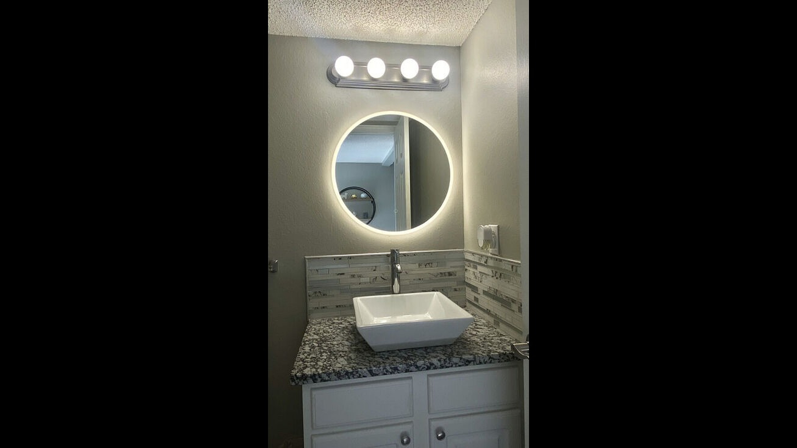 Contemporary bathroom vanity with granite countertop and illuminated mirror.