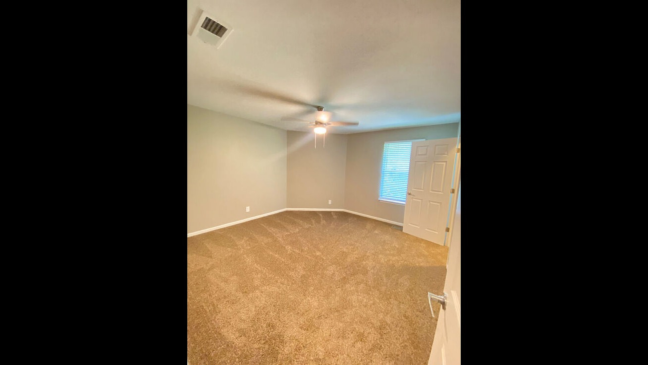 Bright and spacious carpeted bedroom with modern ceiling fan and natural light.
