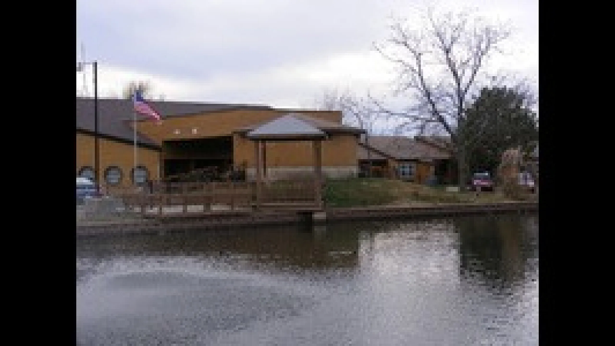 Charming rustic building by a tranquil lake with a wooden gazebo and gently rippling water.