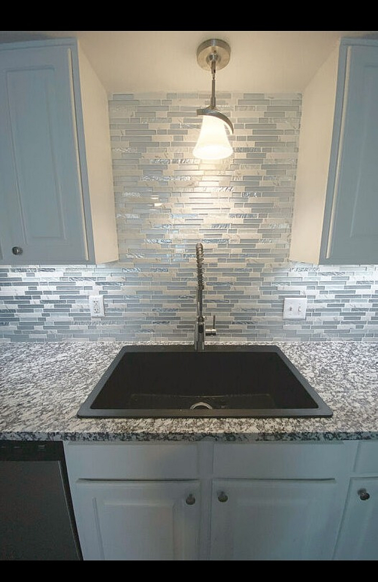 Contemporary kitchen sink setup with mosaic tile backsplash and modern lighting.