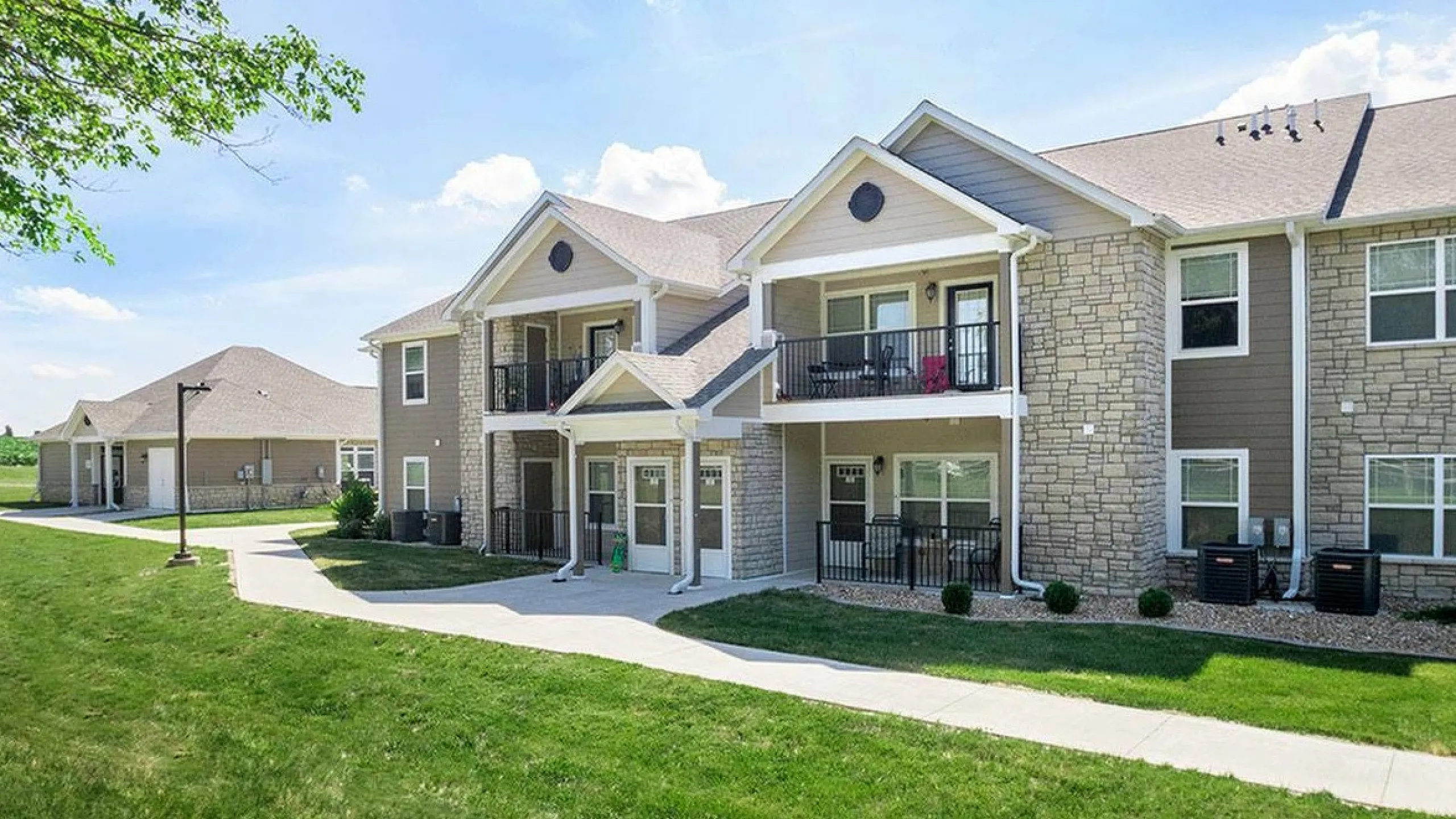 Beautiful two-story apartment complex with stone facade, balconies, and lush green surroundings.