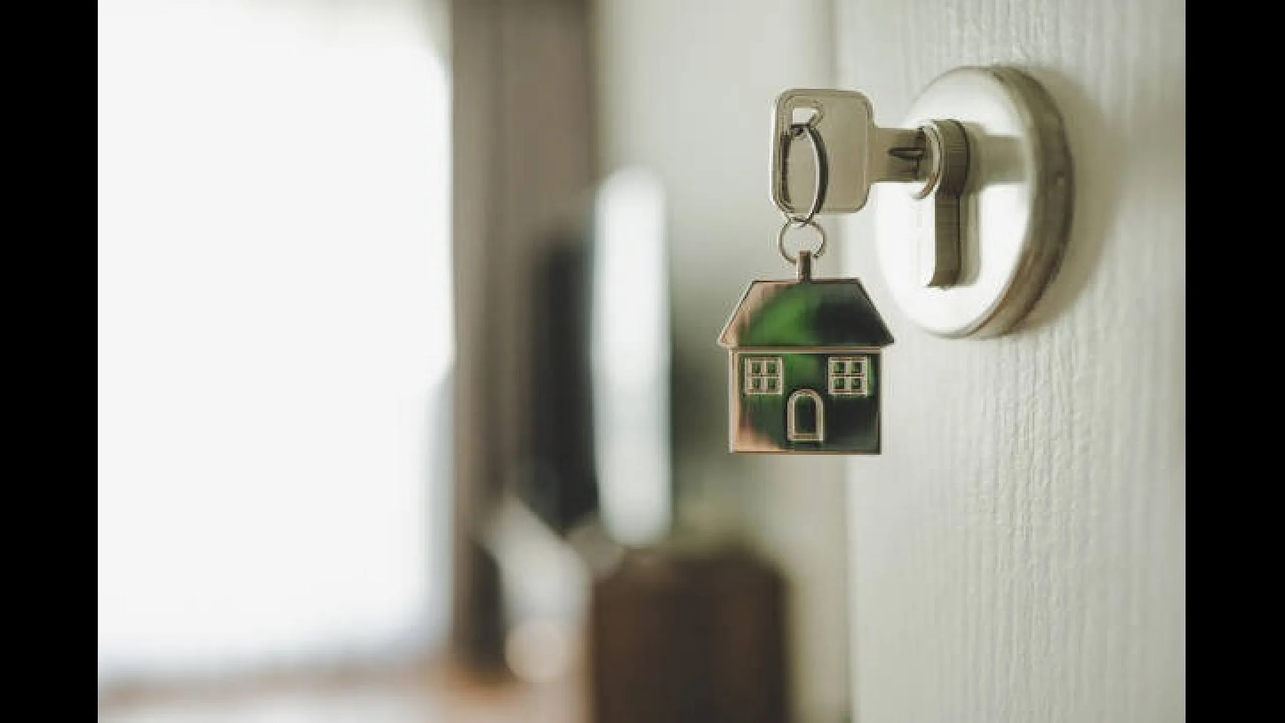Close-up of a key in a door lock, featuring a house-shaped keychain symbolizing new home ownership.
