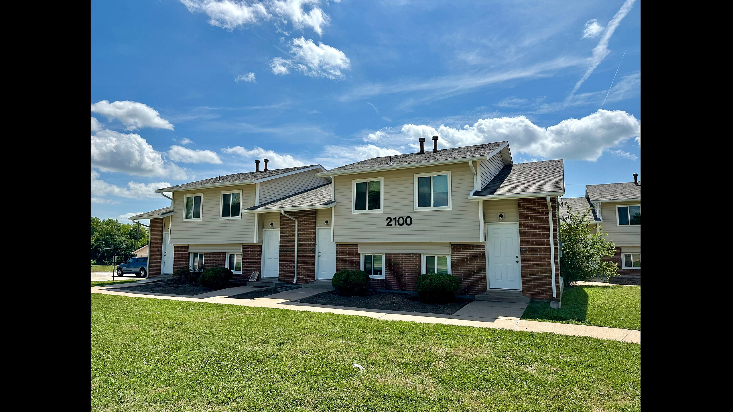 Charming two-story apartment building with brick fa&ccedil;ade, nestled in a lush green neighborhood under a bright blue sky.