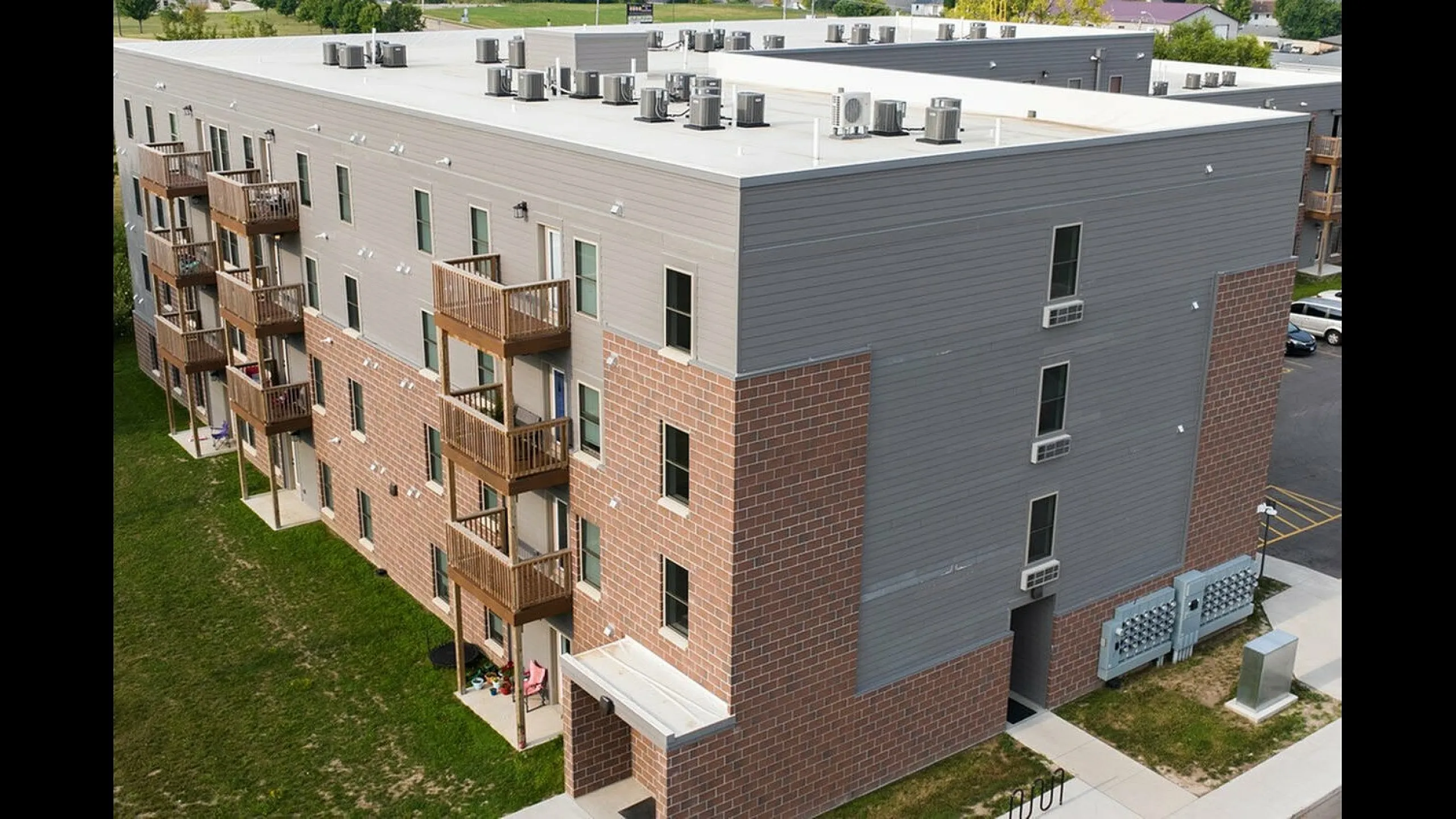 Modern four-story apartment building with attractive brick and siding facade, featuring private balconies and lush green surroundings.