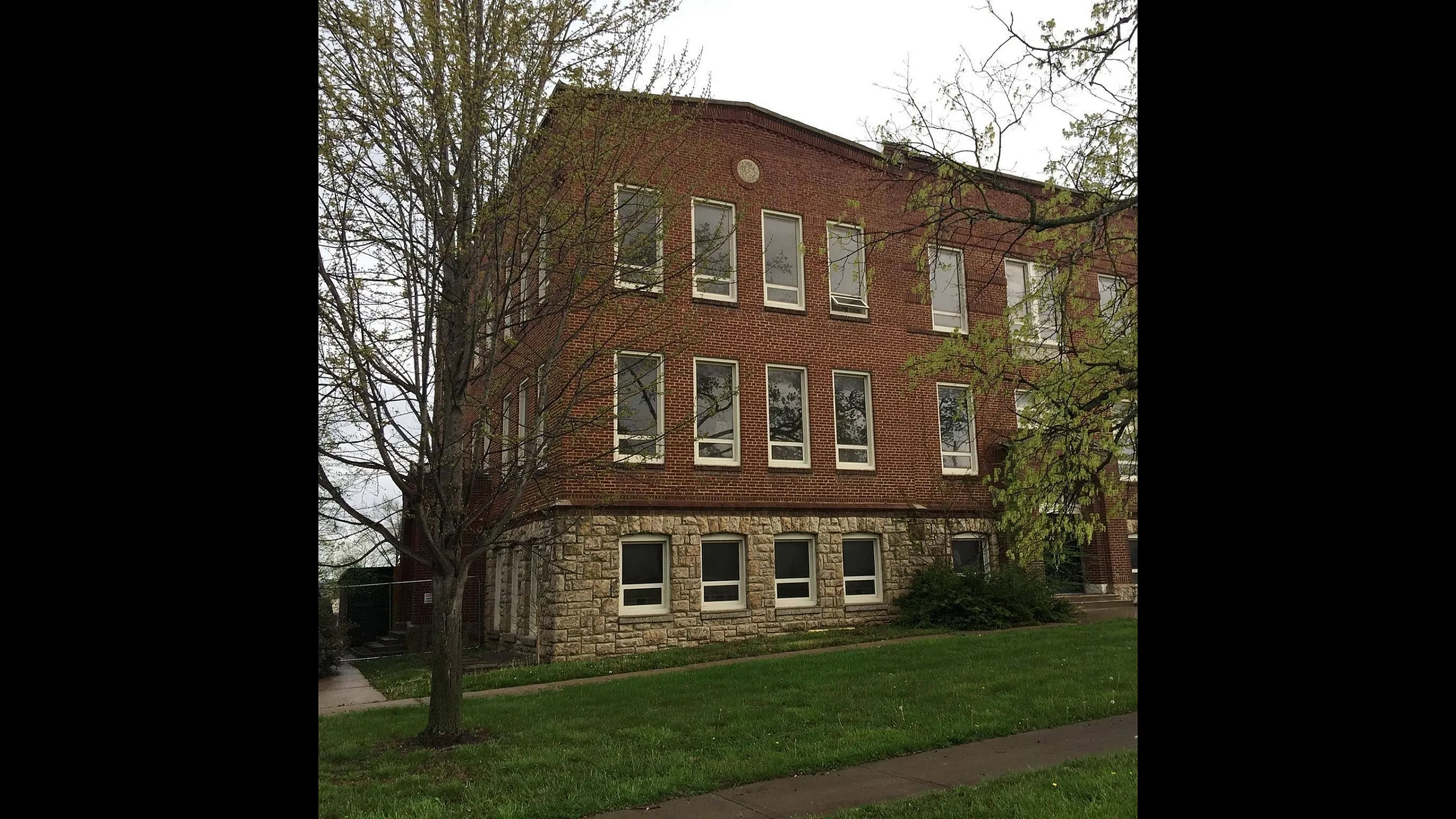 Charming brick building with large windows, nestled in a lush green setting, perfect for modern living.