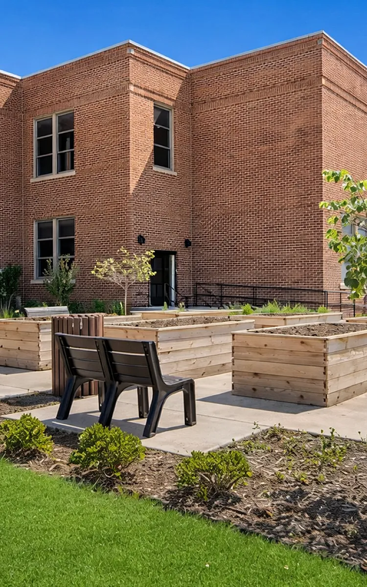 Charming brick building showcasing a lush courtyard with modern seating and raised garden beds for a serene outdoor experience.
