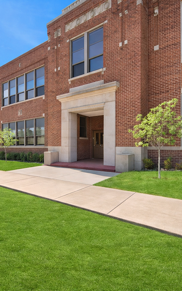 Charming red brick building with large windows and a welcoming entrance, surrounded by lush green lawn and pathways.