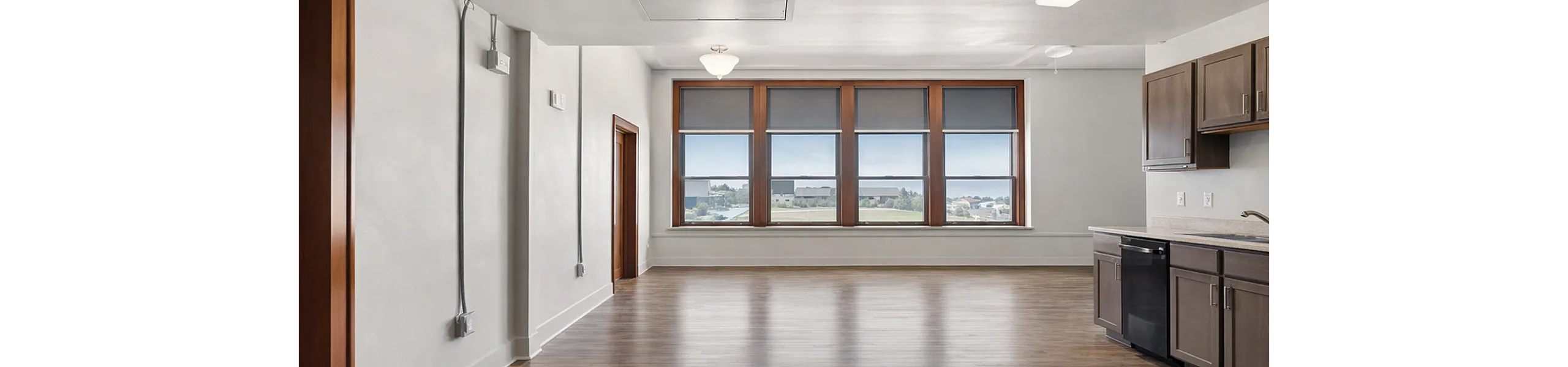 Bright and spacious living area with large windows offering scenic views, sleek hardwood floors, and a modern kitchen in an open-plan design.