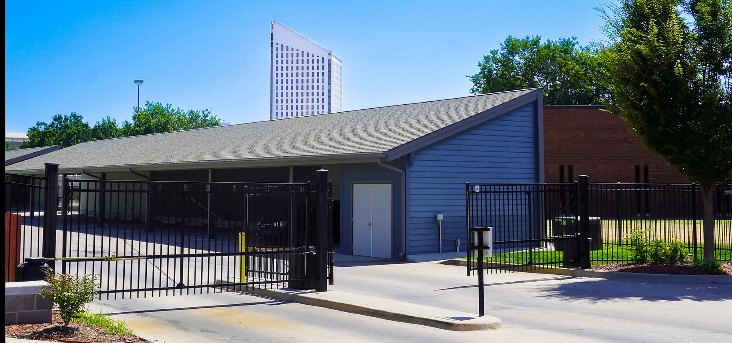 Inviting modern property with secure gated entry, featuring sleek architecture and lush greenery, set against a vibrant blue sky.