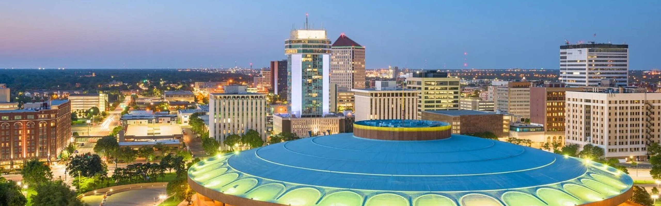 Vibrant cityscape at dusk showcasing modern architecture with illuminated buildings and spacious urban layout.