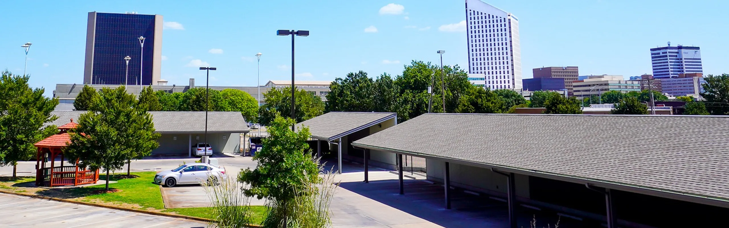 Vibrant cityscape view featuring modern buildings under a clear blue sky, surrounded by lush greenery and well-maintained parking area.