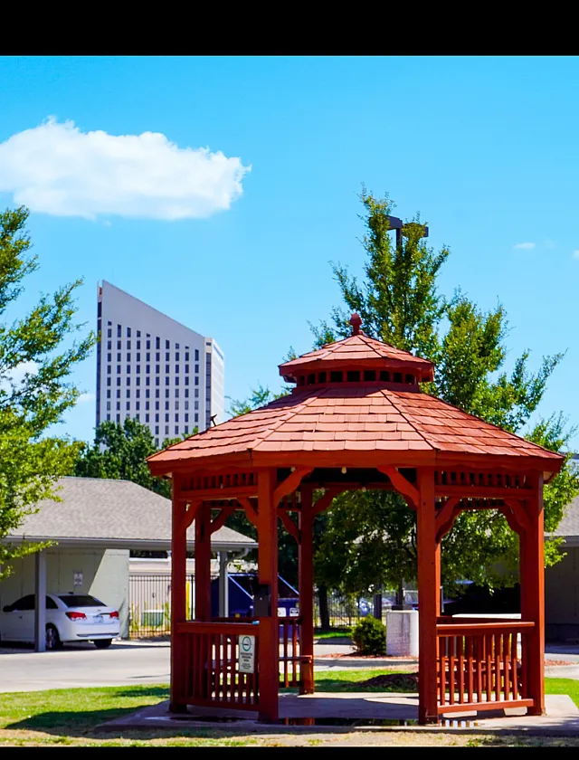 Charming apartment complex featuring a picturesque red wooden gazebo surrounded by lush greenery, ideal for relaxing outdoors.