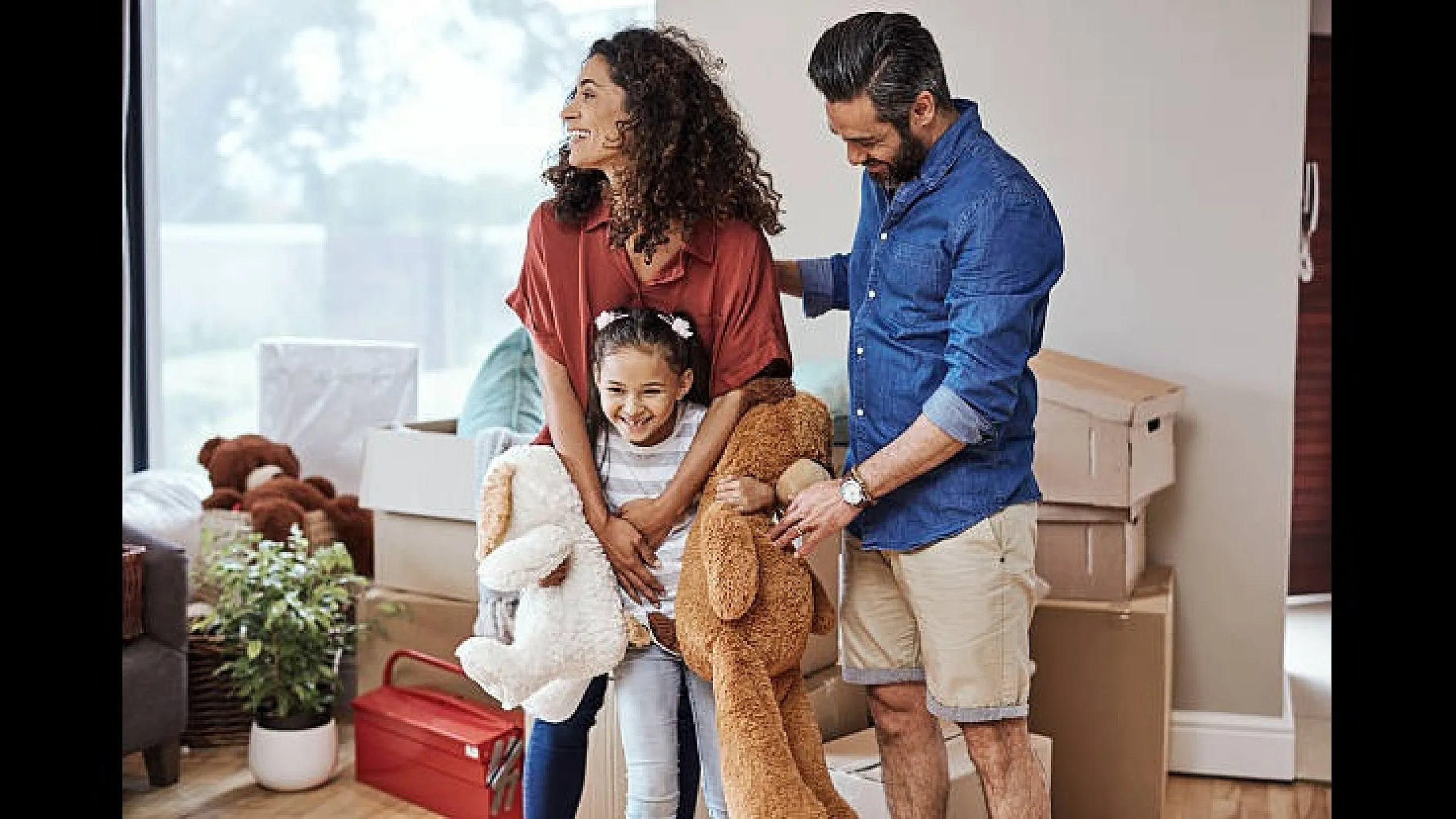 Happy family embracing in a sunlit room surrounded by moving boxes, symbolizing a fresh start in a new apartment.