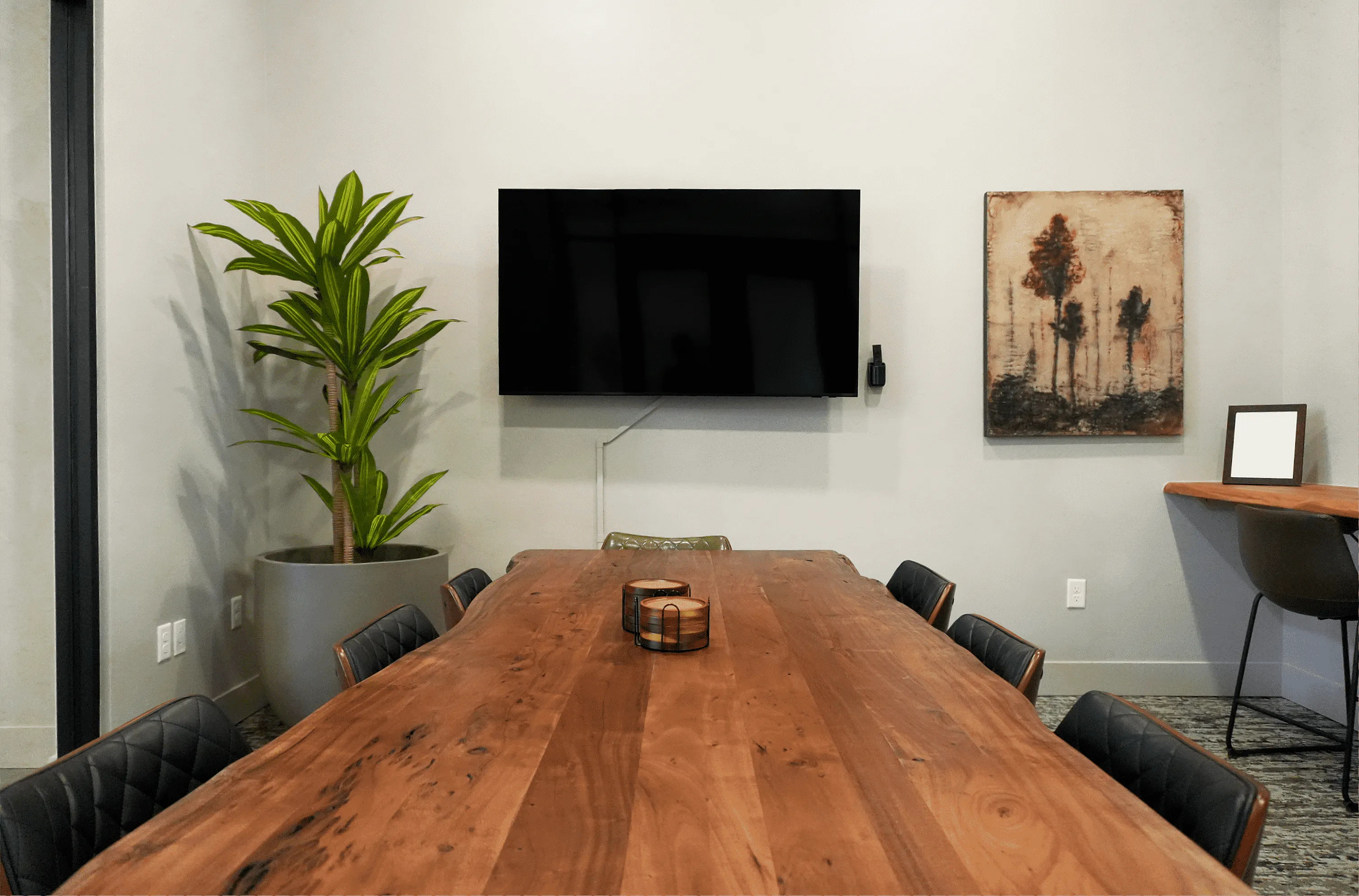 Conference Room with a polished wooden table, modern wall-mounted TV, lush potted plant, and contemporary artwork.