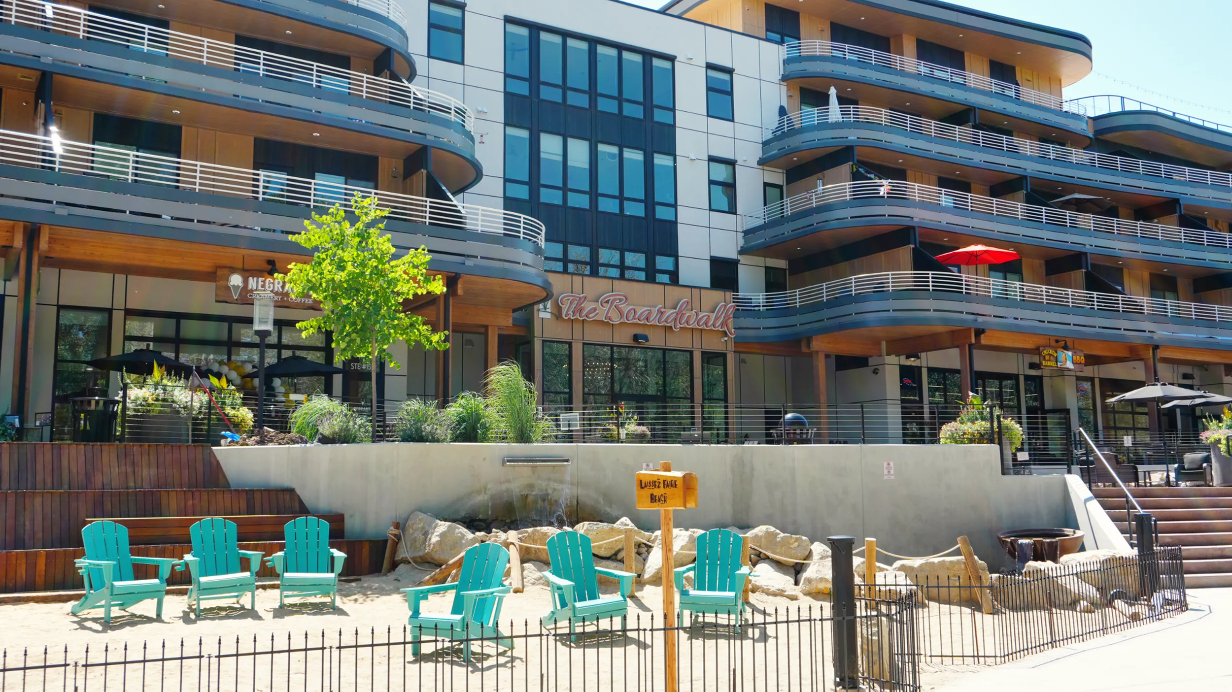 Chic modern apartment complex with elegant balconies, vibrant turquoise chairs, and a beach-themed outdoor setting at 'The Boardwalk'.