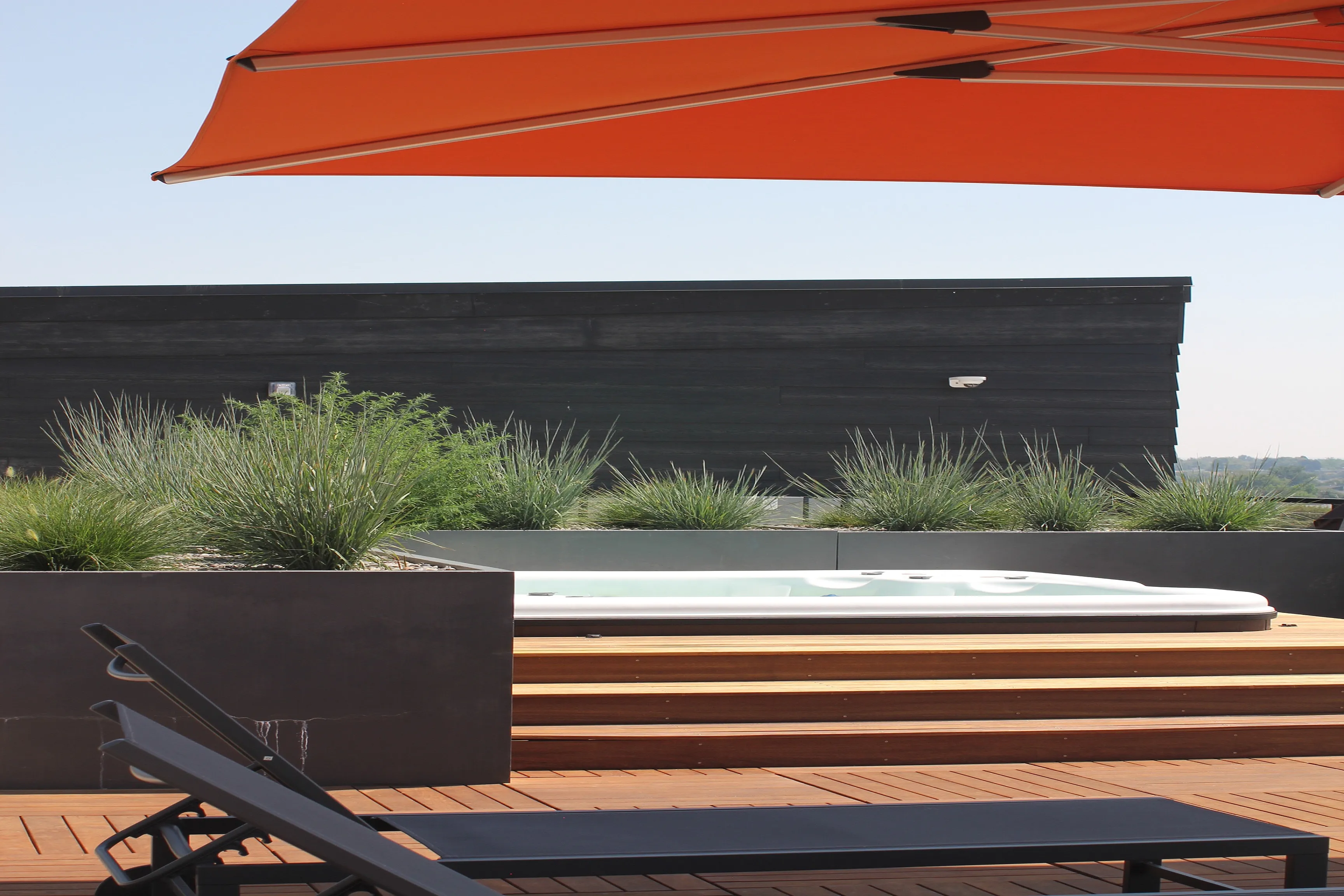 Luxurious rooftop oasis featuring a stylish jacuzzi, modern deck chairs, and lush greenery under a vibrant orange canopy.