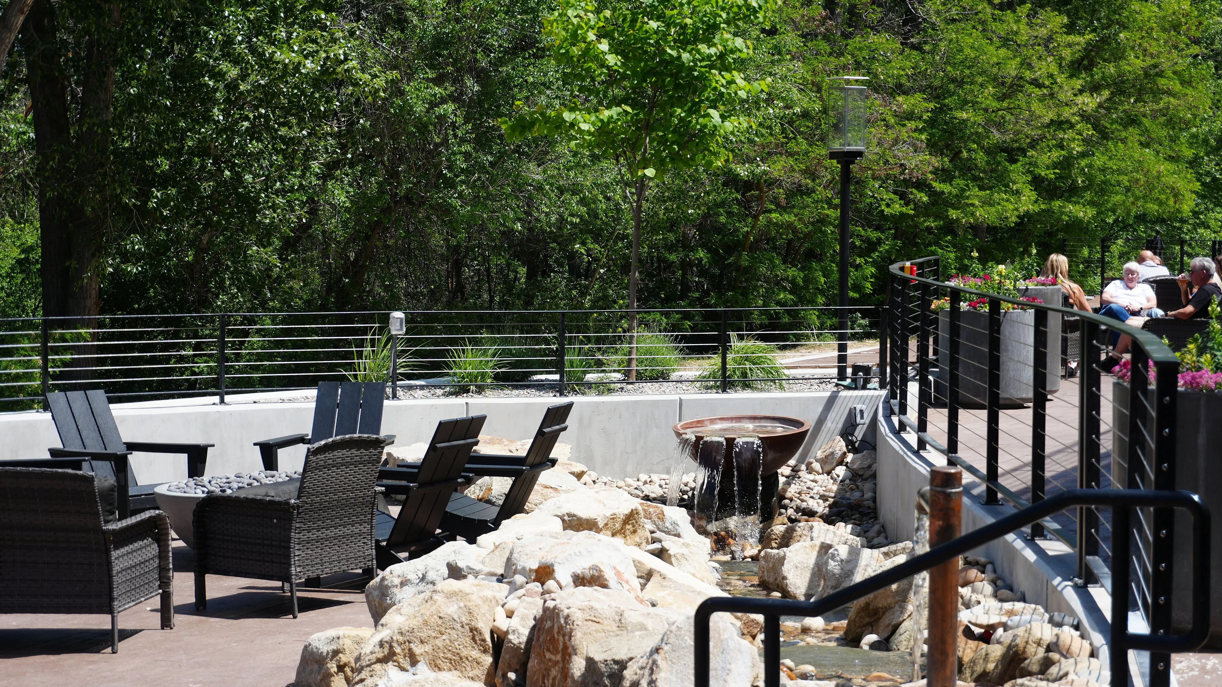 Serene outdoor patio with modern wicker seating, lush greenery, and a tranquil water feature perfect for relaxation.