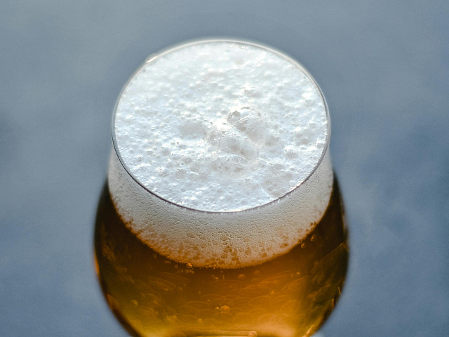Refreshing glass of amber beer with a rich frothy head, set against a sleek gray background.