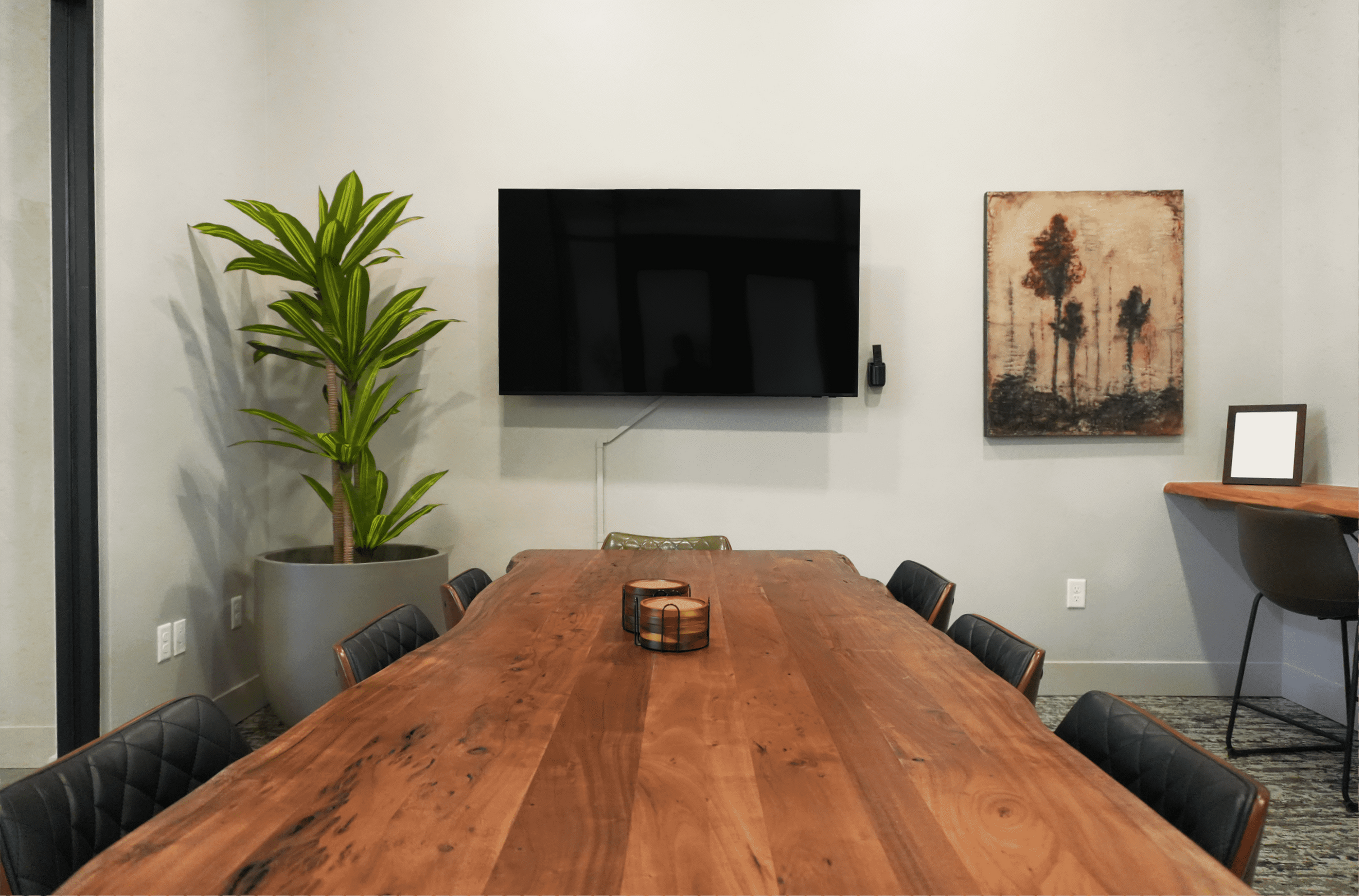 Elegant apartment dining area featuring a long wooden table, modern wall-mounted TV, vibrant potted plant, and contemporary artwork.