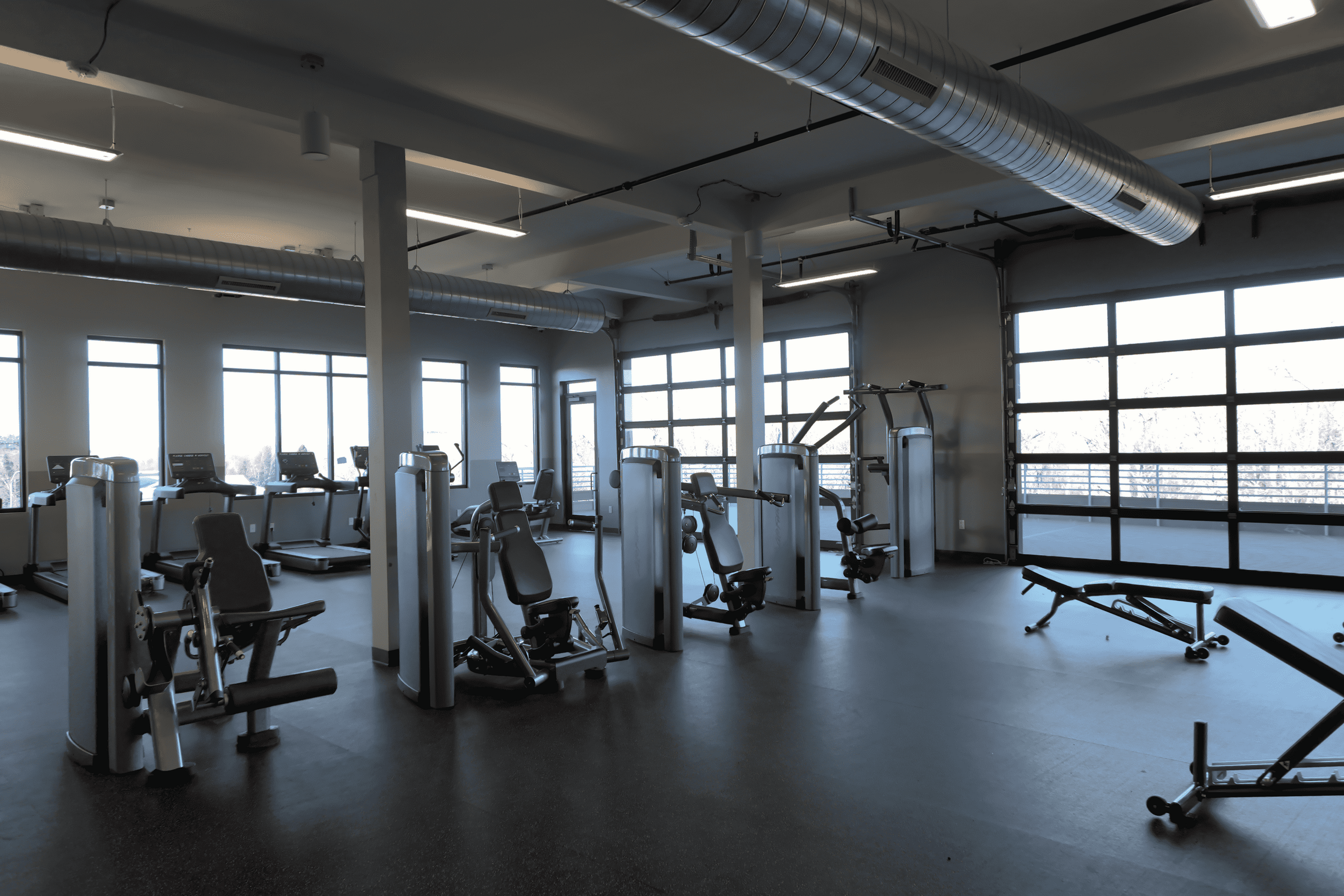 Spacious gym with modern fitness equipment and large windows offering plenty of natural light.