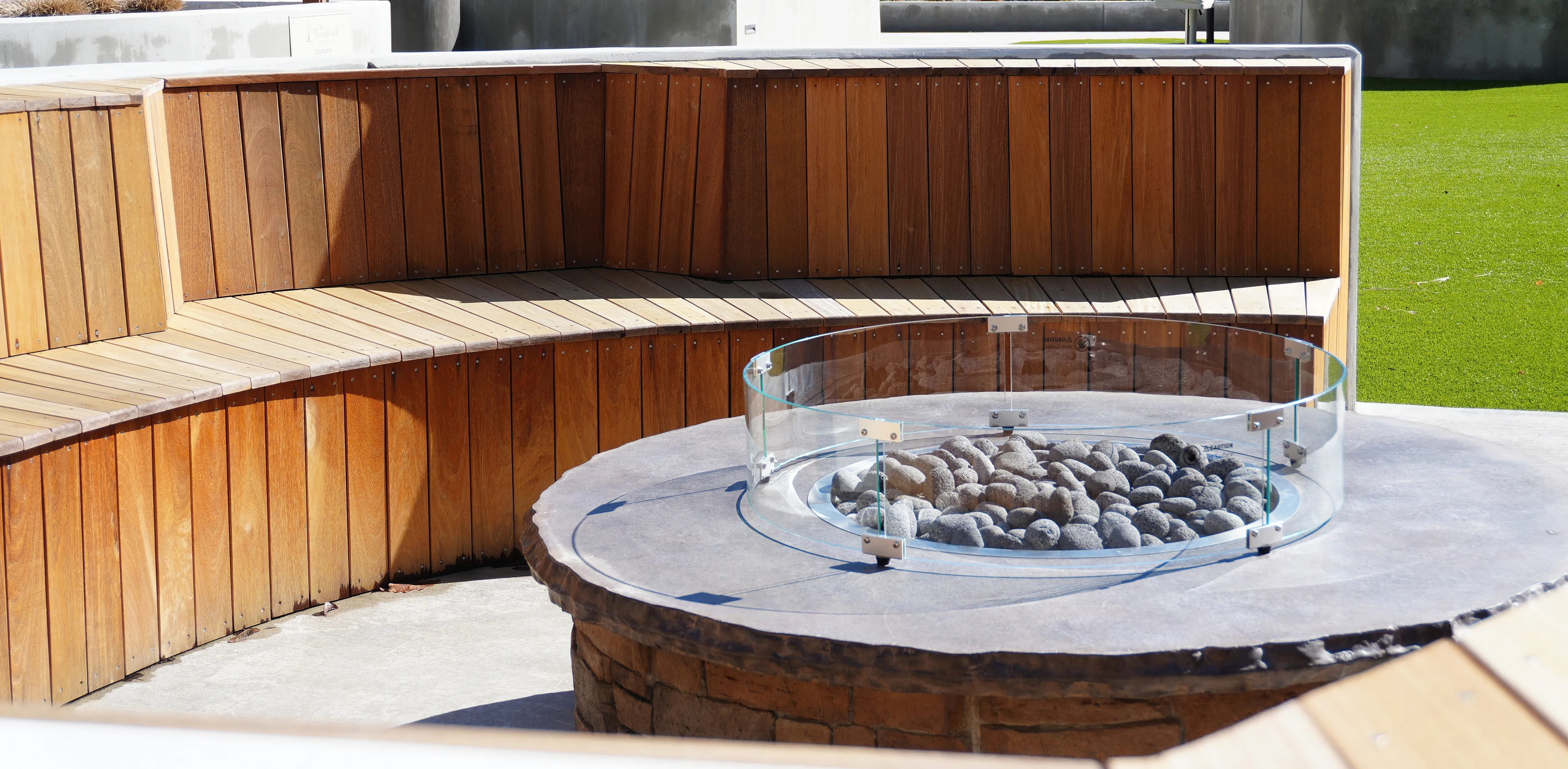 Inviting outdoor seating area featuring curved wooden benches and a modern glass-encased fire pit, perfect for social gatherings.