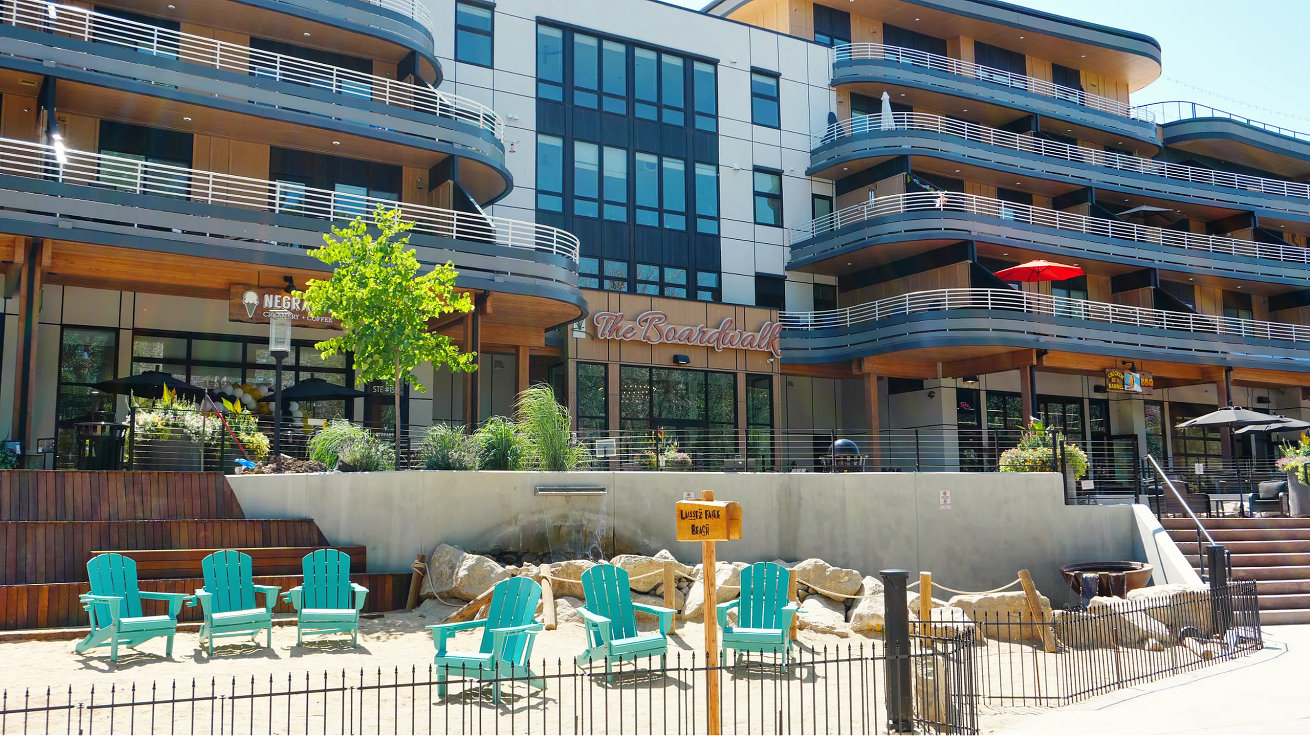 Modern apartment complex with stylish balcony designs and outdoor seating area, featuring turquoise chairs and lush landscaping.