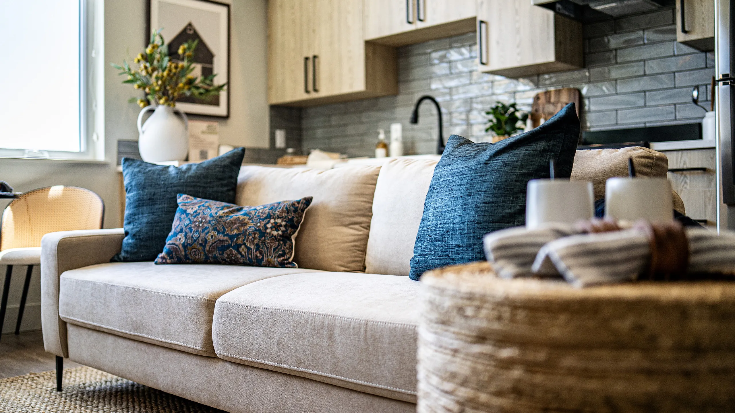 Chic living area with a cozy beige sofa, stylish throw pillows, and modern kitchen backdrop.