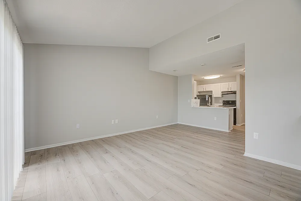 Bright, open-plan living area with stylish light wood flooring, seamlessly connected to a modern kitchen featuring sleek white cabinetry and stainless steel appliances.