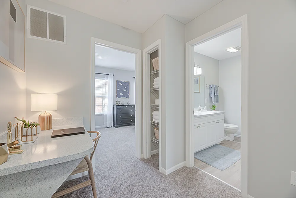 Inviting hallway with a stylish workspace leading to a cozy bedroom and bright bathroom, showcasing modern design and ample natural light.