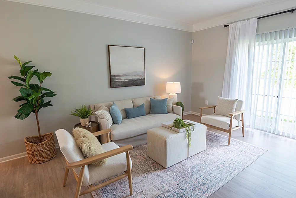 Inviting living room with modern decor, large window, stylish furniture, and lush plant accents.