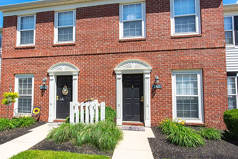 Charming brick townhouse facade with welcoming black doors, large windows, and lush greenery, ideal for modern living.