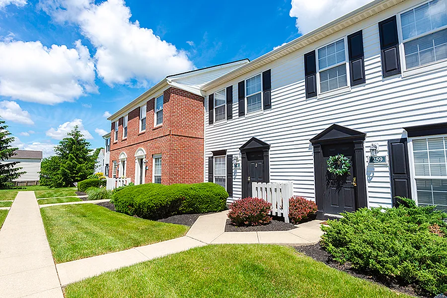 Charming townhouse exterior with brick and siding facade, nestled in beautifully manicured gardens under a bright blue sky.