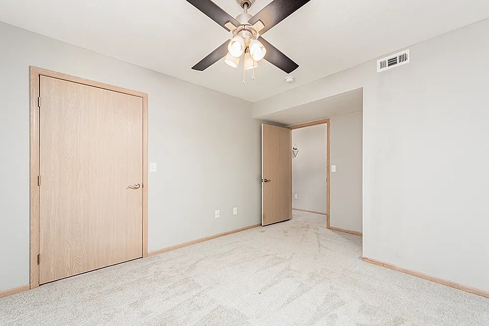 Bright and modern bedroom with plush carpet, neutral walls, and elegant ceiling fan in a chic apartment.