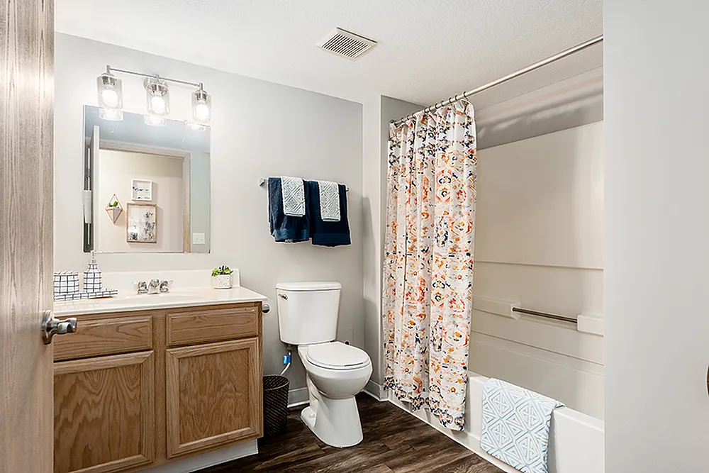 Bright, inviting bathroom featuring elegant lighting, chic shower curtain, and stylish wood cabinetry.
