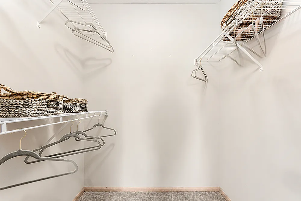 Spacious walk-in closet with organized shelving, elegant hangers, and stylish woven baskets. Perfect for storage and accessibility in any modern apartment.