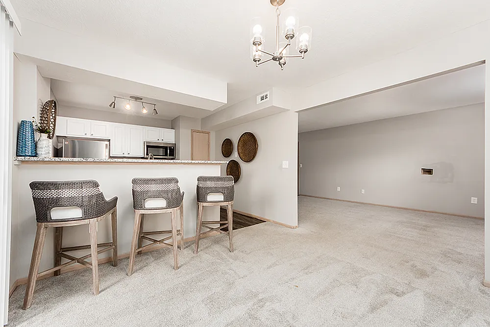 Inviting open-concept kitchen with stylish bar seating and modern lighting, leading into a spacious, carpeted living area.