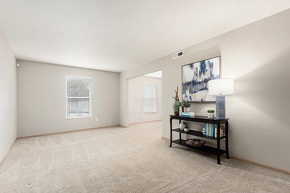 Inviting living room with plush carpet, modern decor, and flawless natural light from large window.