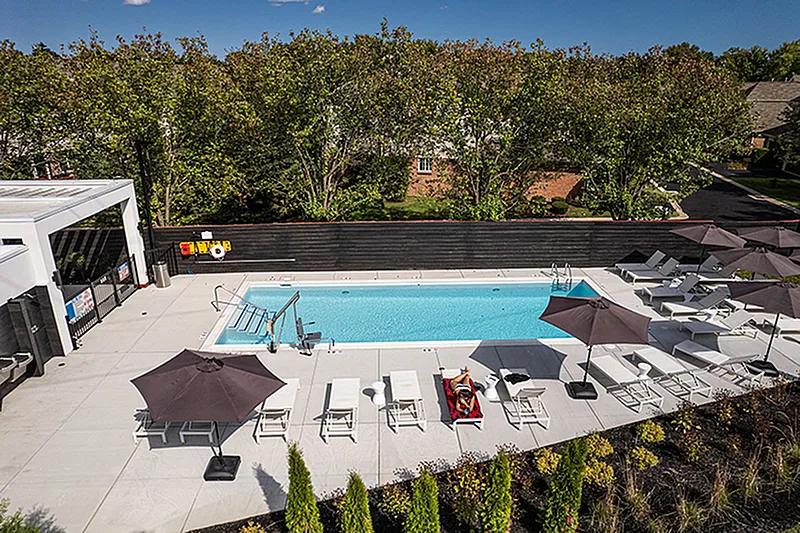 Luxurious outdoor pool area with modern lounge chairs and umbrellas, surrounded by lush greenery, perfect for relaxation and summer enjoyment.