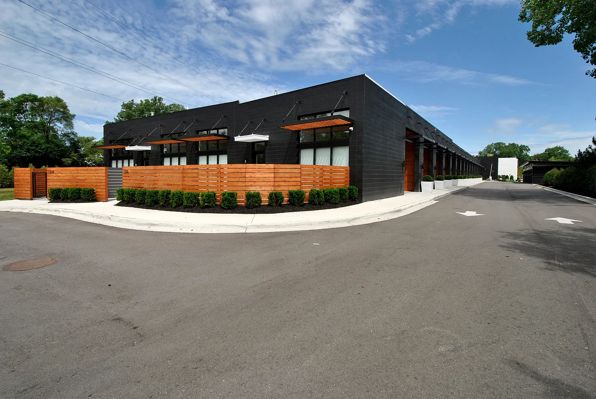Modern industrial building featuring sleek black facade with decorative wooden accents and neatly landscaped greenery on a spacious lot.