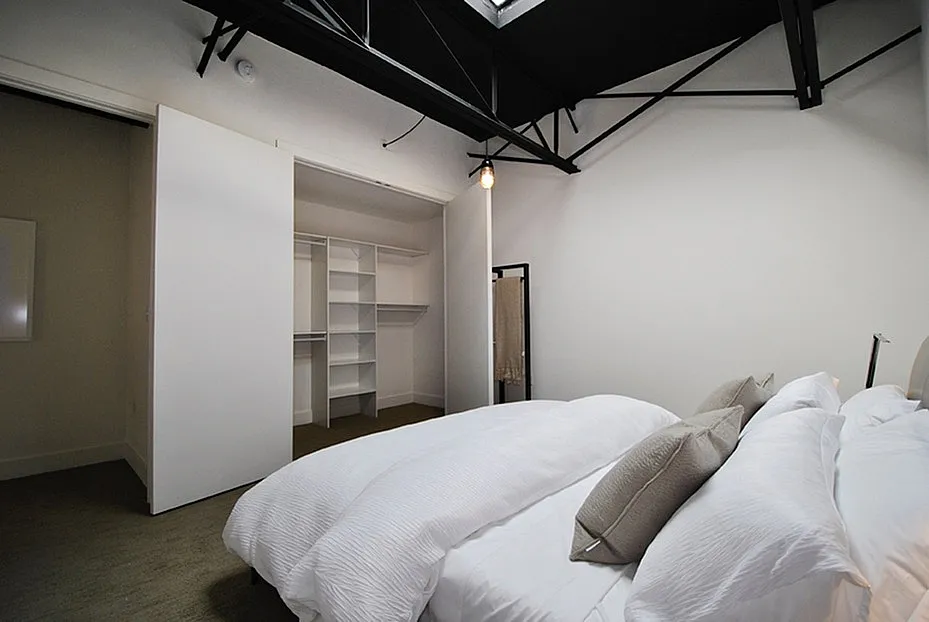 Modern bedroom with skylight, white bedding, and spacious walk-in closet for an airy and inviting atmosphere.
